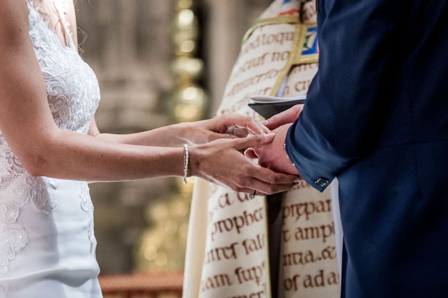 Close-up of hands during wedding ceremony exchange in ornate church setting.