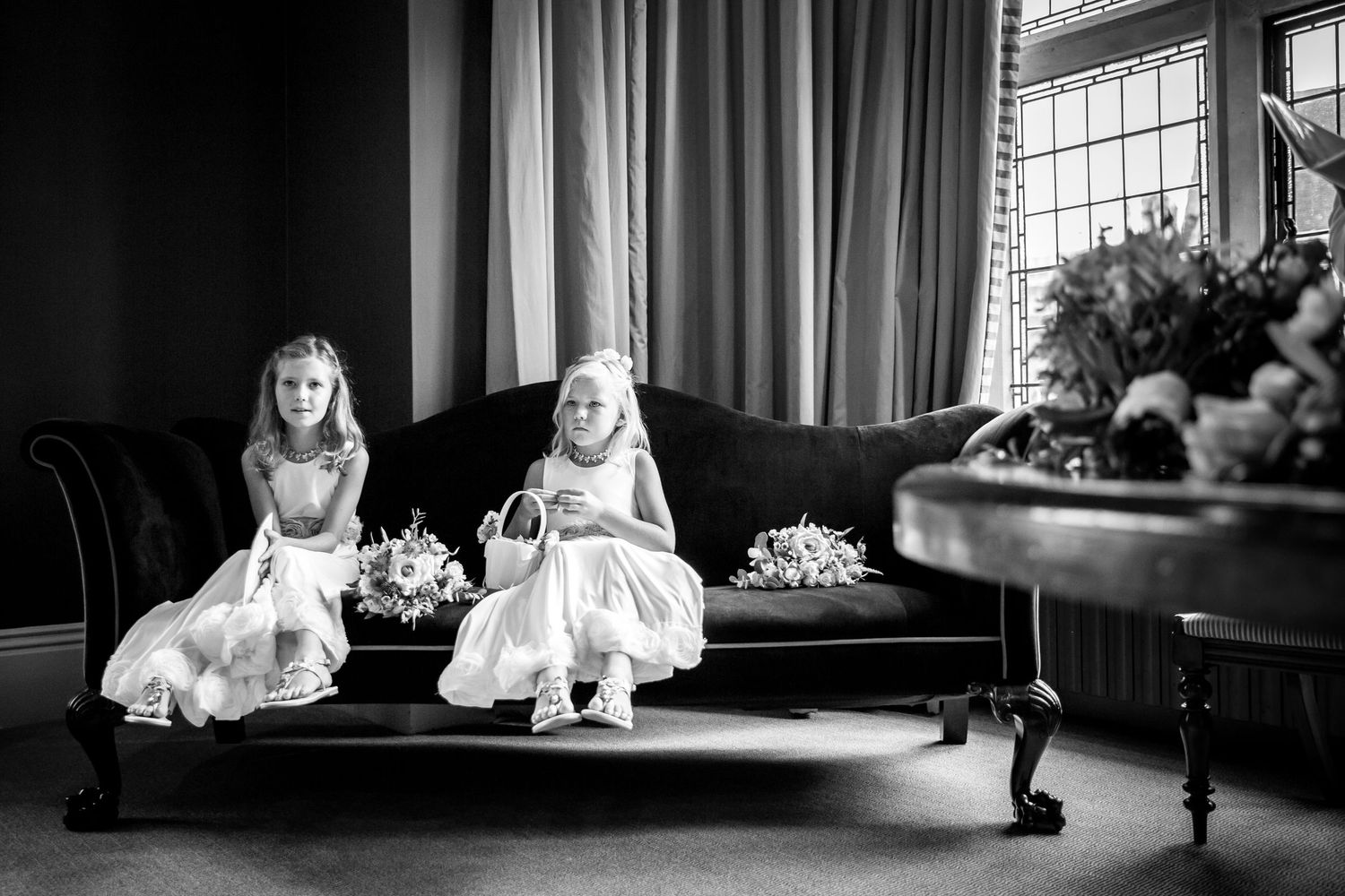 Black and white photo of two young flower girls sitting on vintage sofa.