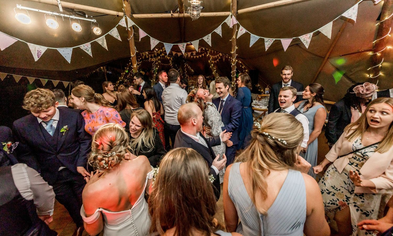 Wedding reception dance floor filled with guests celebrating under white bunting decorations.
