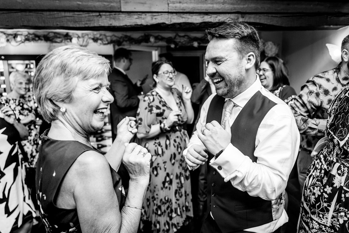 Black and white candid photo of dancing and laughter at reception party.
