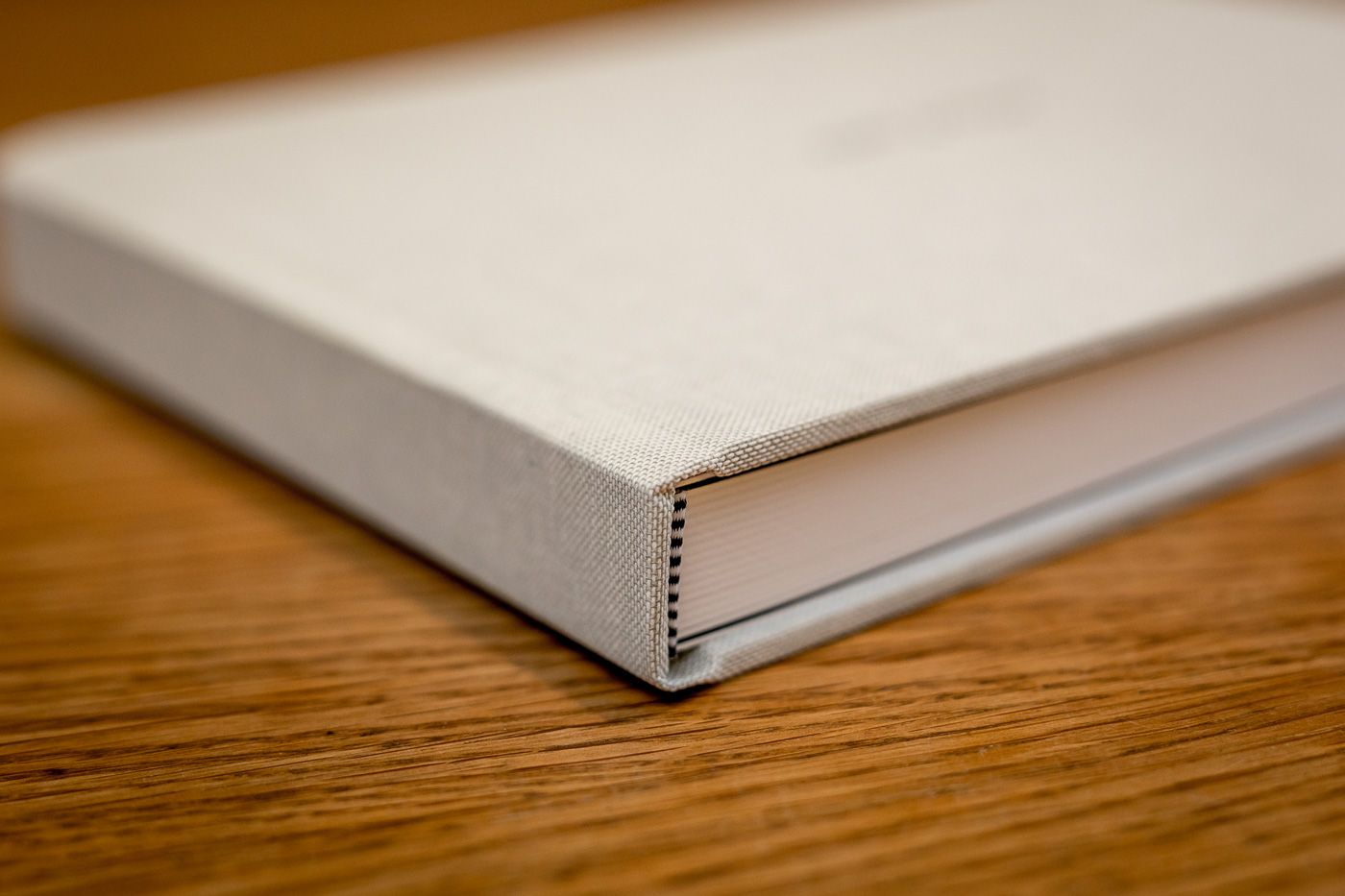 A close-up view of a hardcover book spine showing minimal white binding details against a wooden surface.