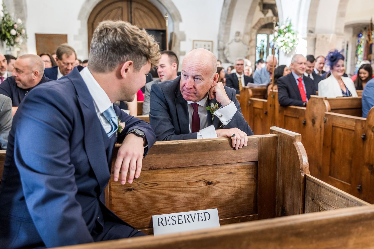 Wedding ceremony taking place in traditional church with wooden pews and reserved seating signs.
