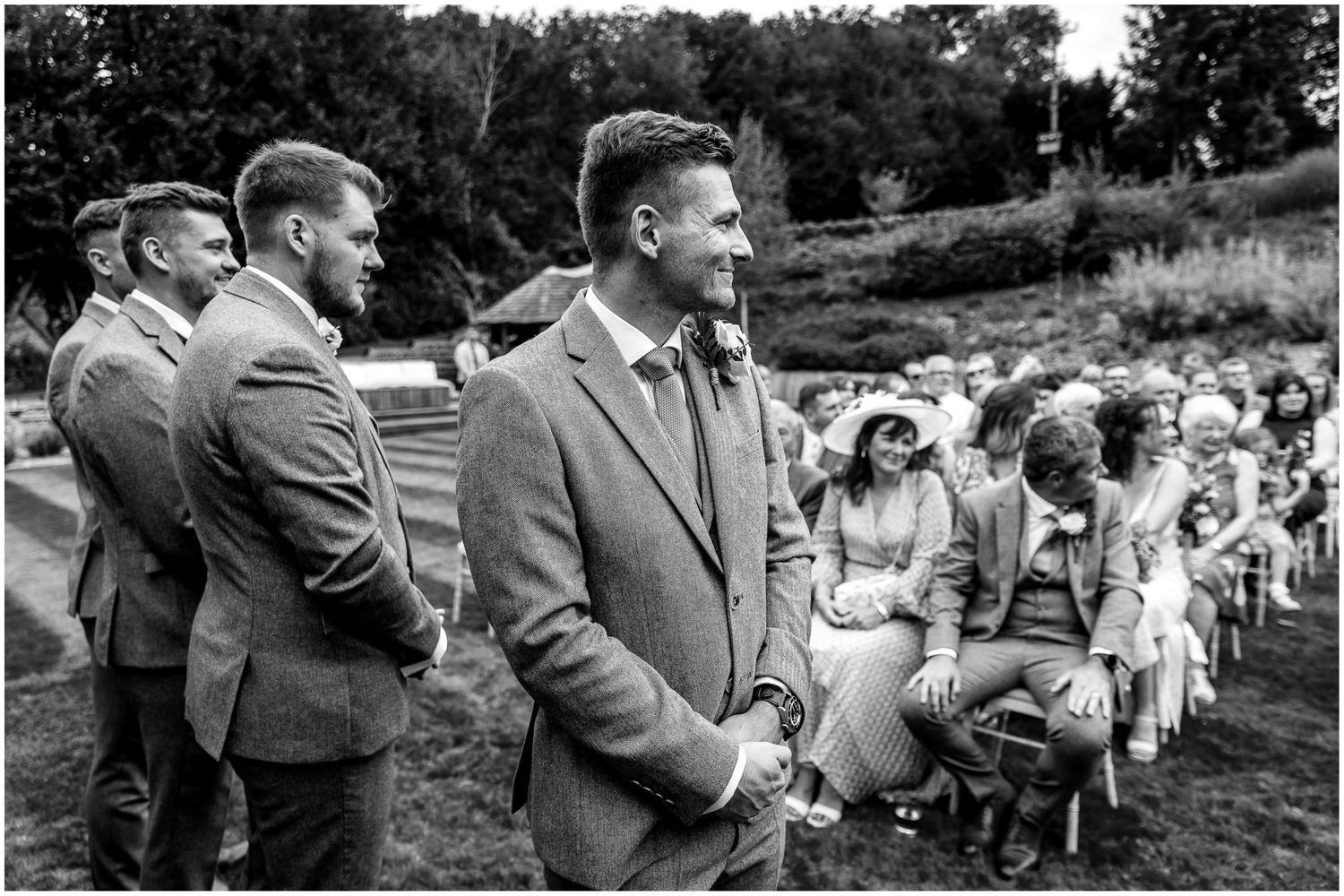 Black and white panorama of wedding guests seated outdoors during ceremony.