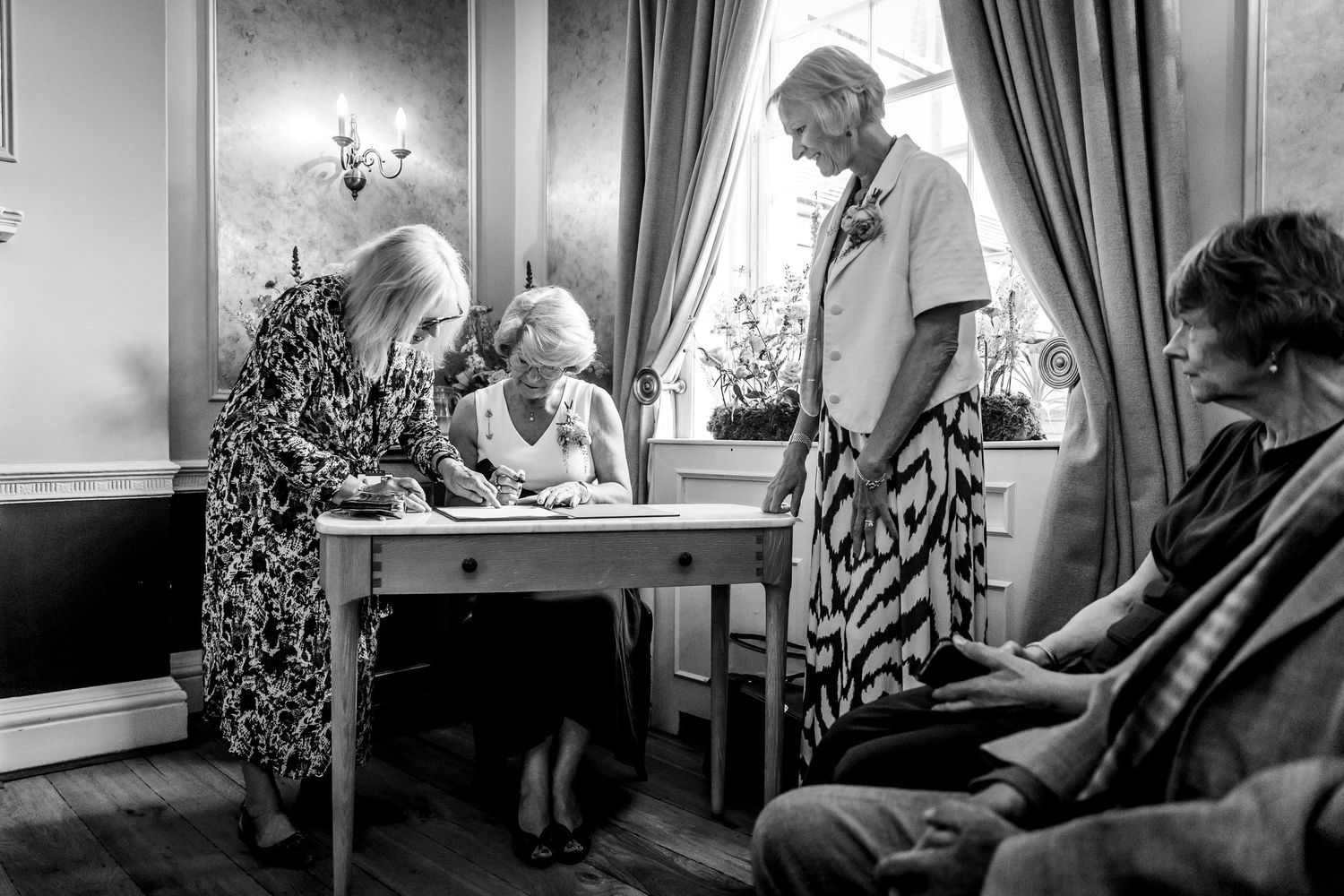 Elderly couple signing documents together at a table in an elegant room with curtains.