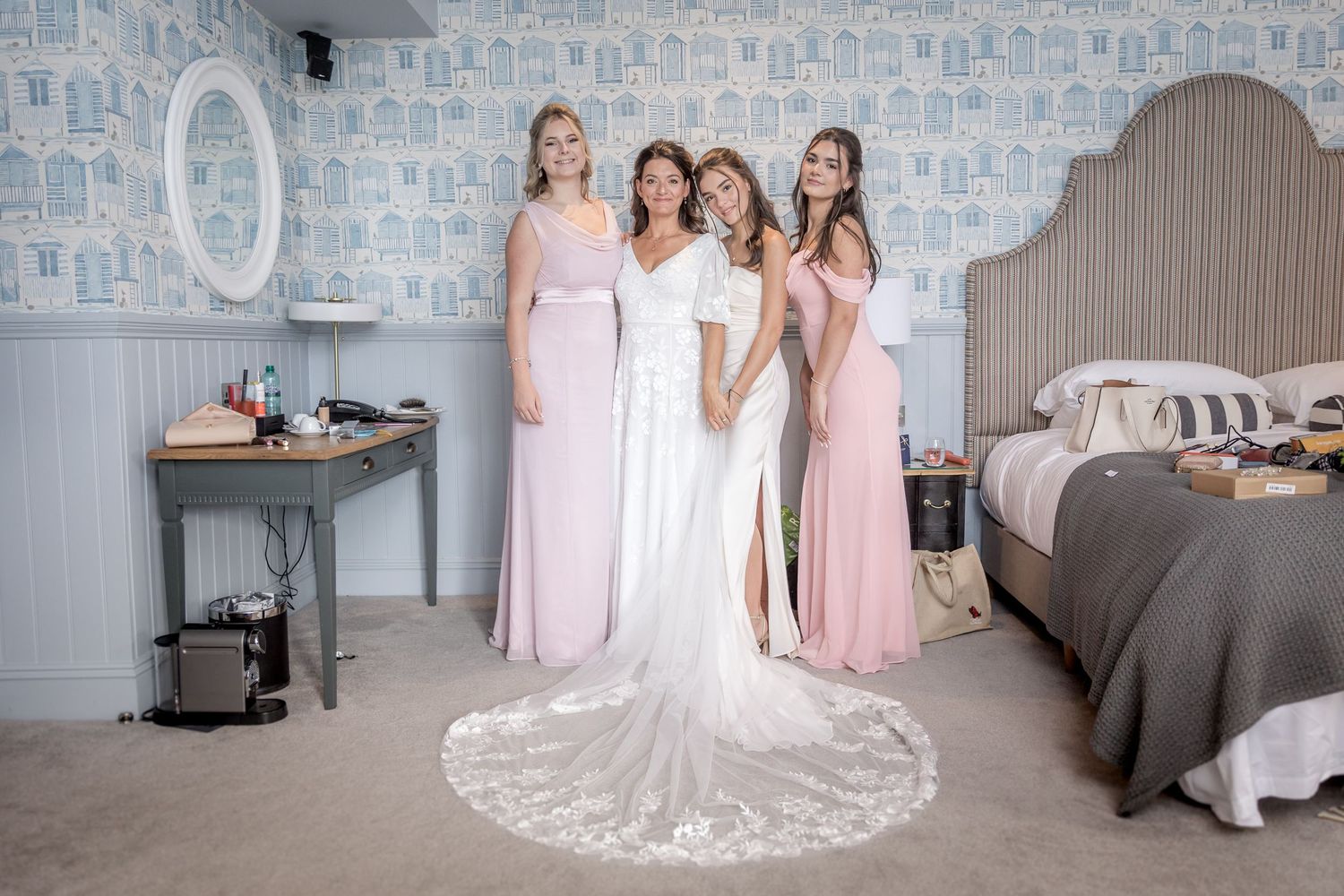 Bridal party in white and pink dresses posing against blue patterned wallpaper.