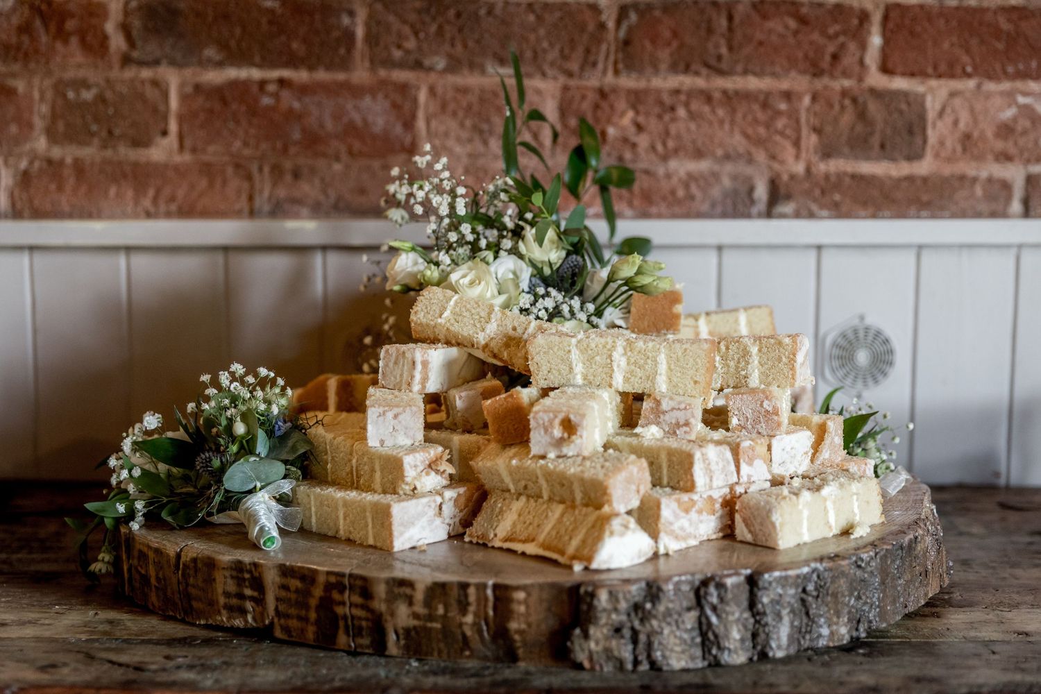 Row of rustic wedding favors displayed on wooden table against brick wall.