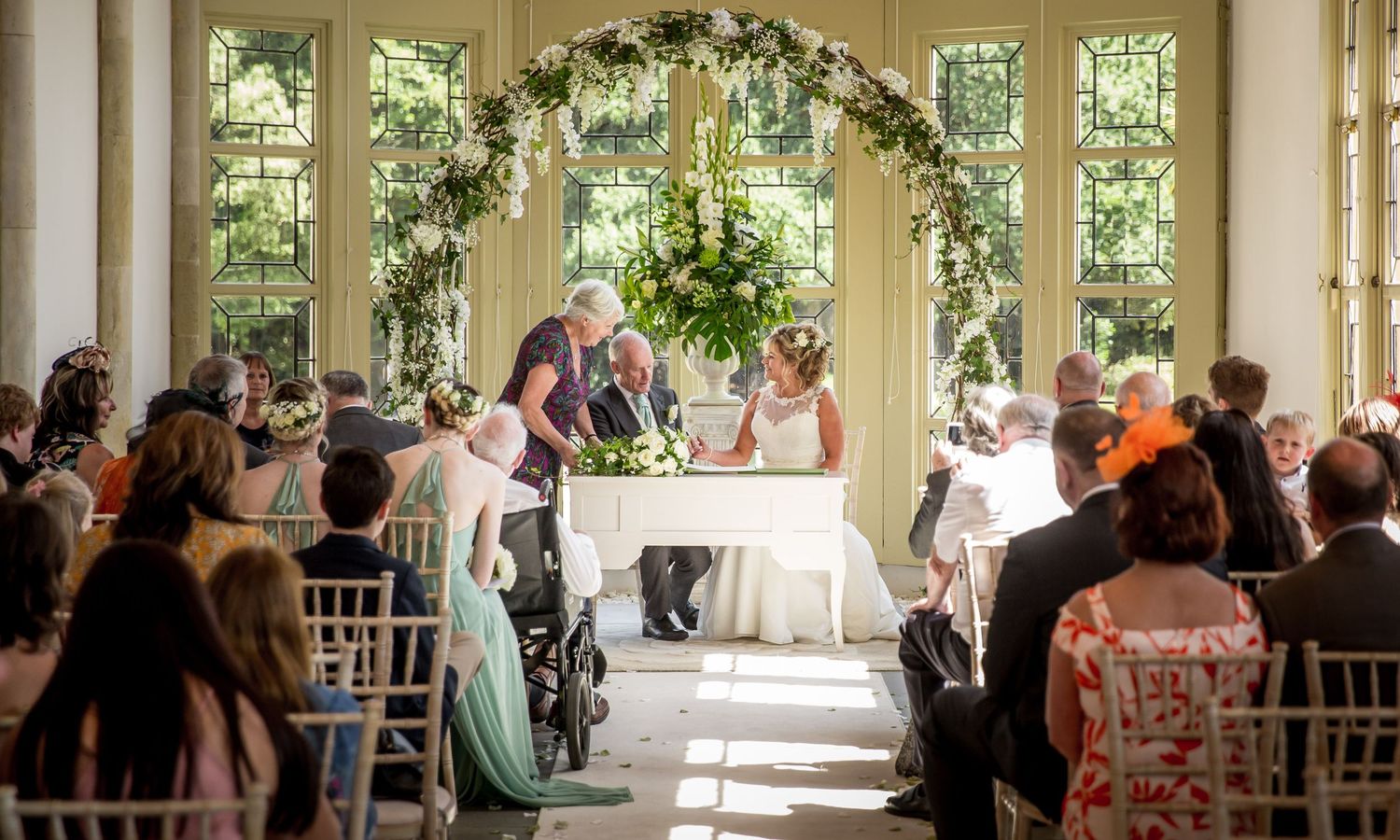 A bride and groom sign the register during the wedding ceremony in the Winter Garden room at Highcliffe Castle in the New Forest.
