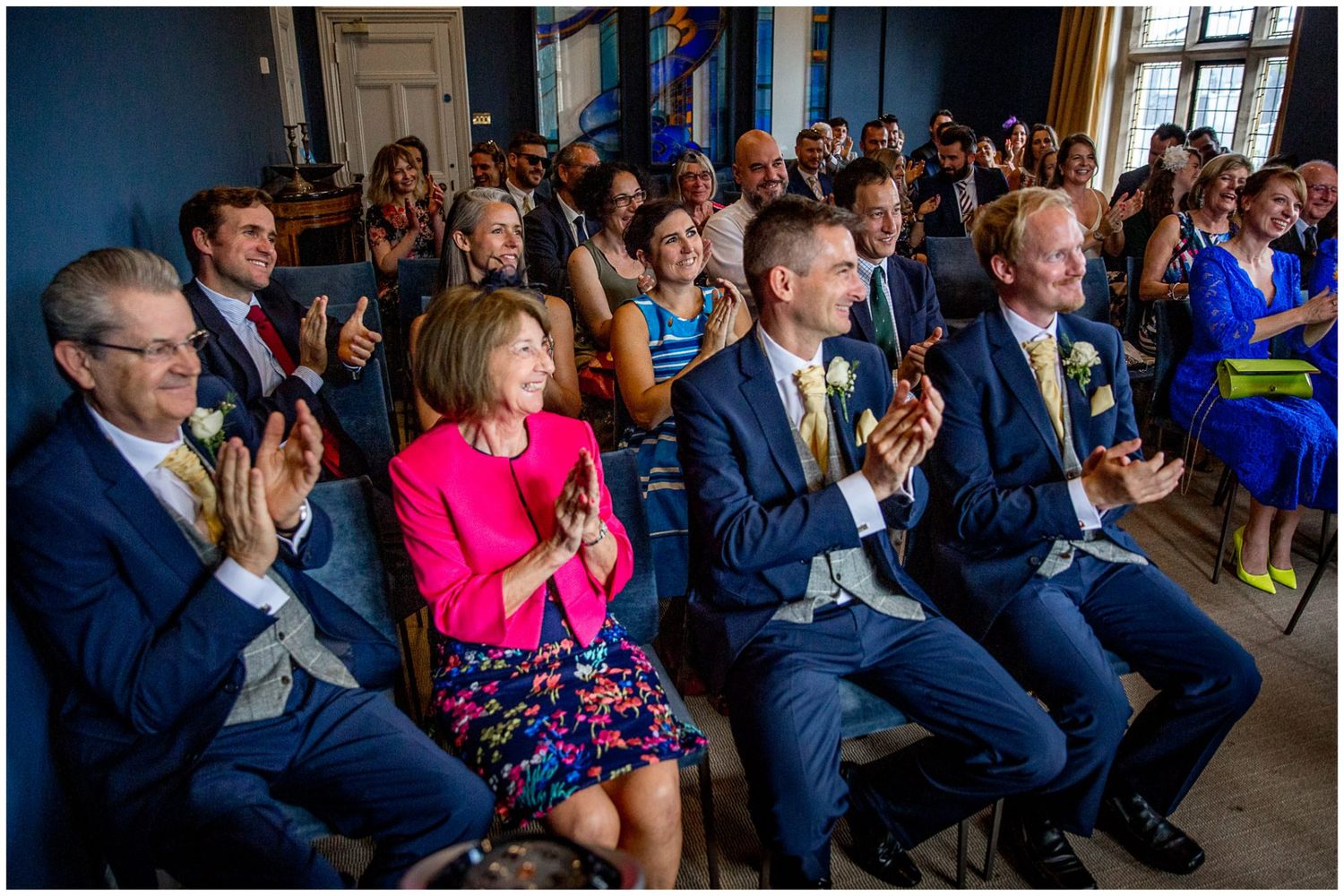 Wedding guests seated in rows watch and react emotionally during an indoor ceremony.