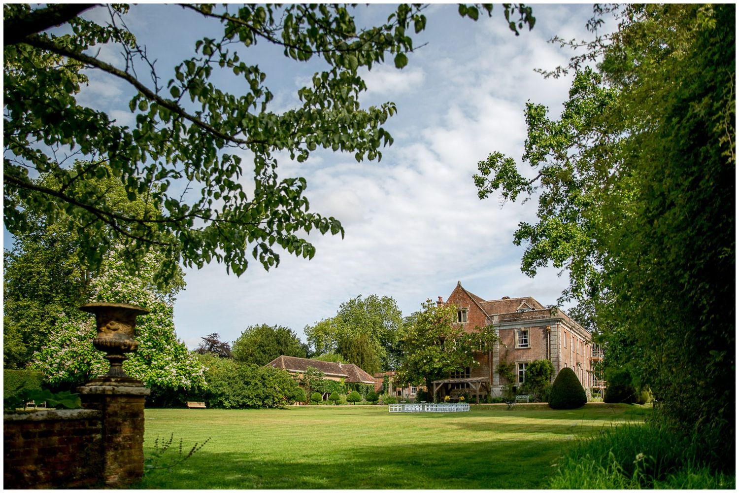 A panoramic view of a historic brick mansion surrounded by lush green lawns and mature trees on a sunny day.