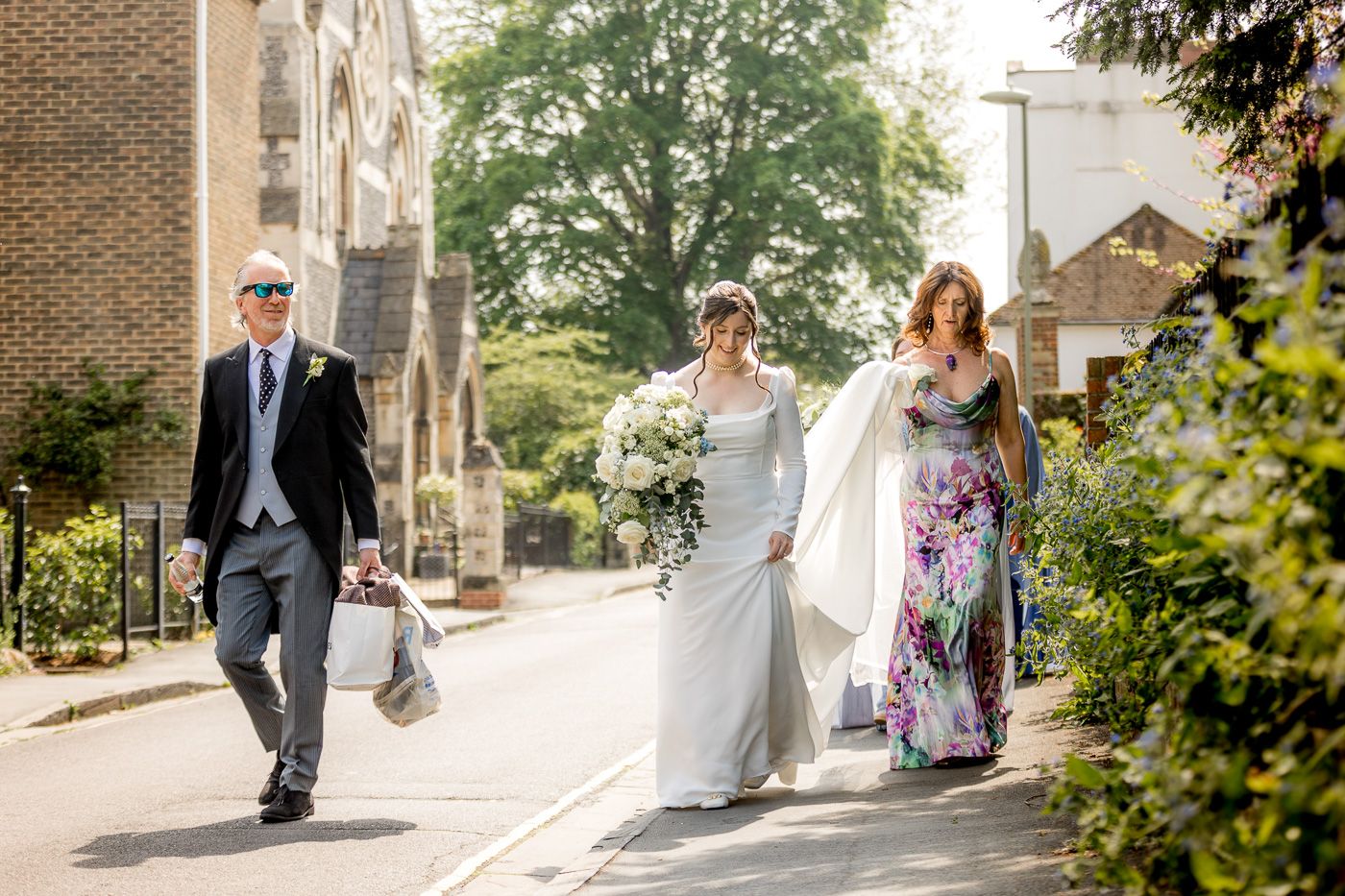Wedding party walking along brick building exterior in natural daylight.