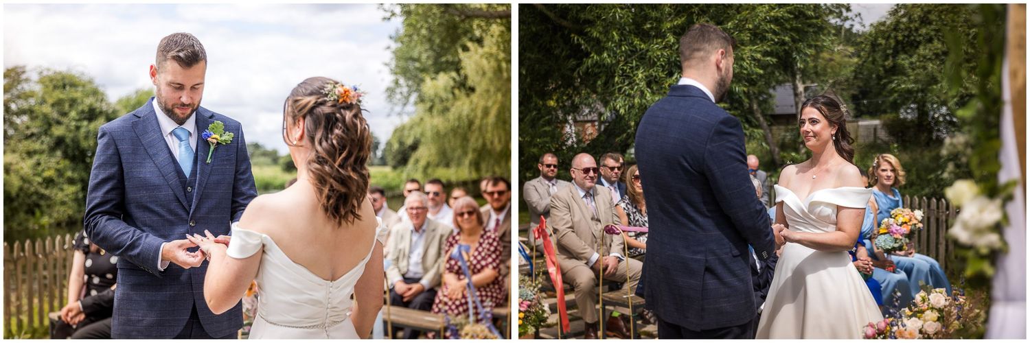 Groom places wedding ring on brides finger during  a Sopley Mill outdoor ceremony while guests watch.