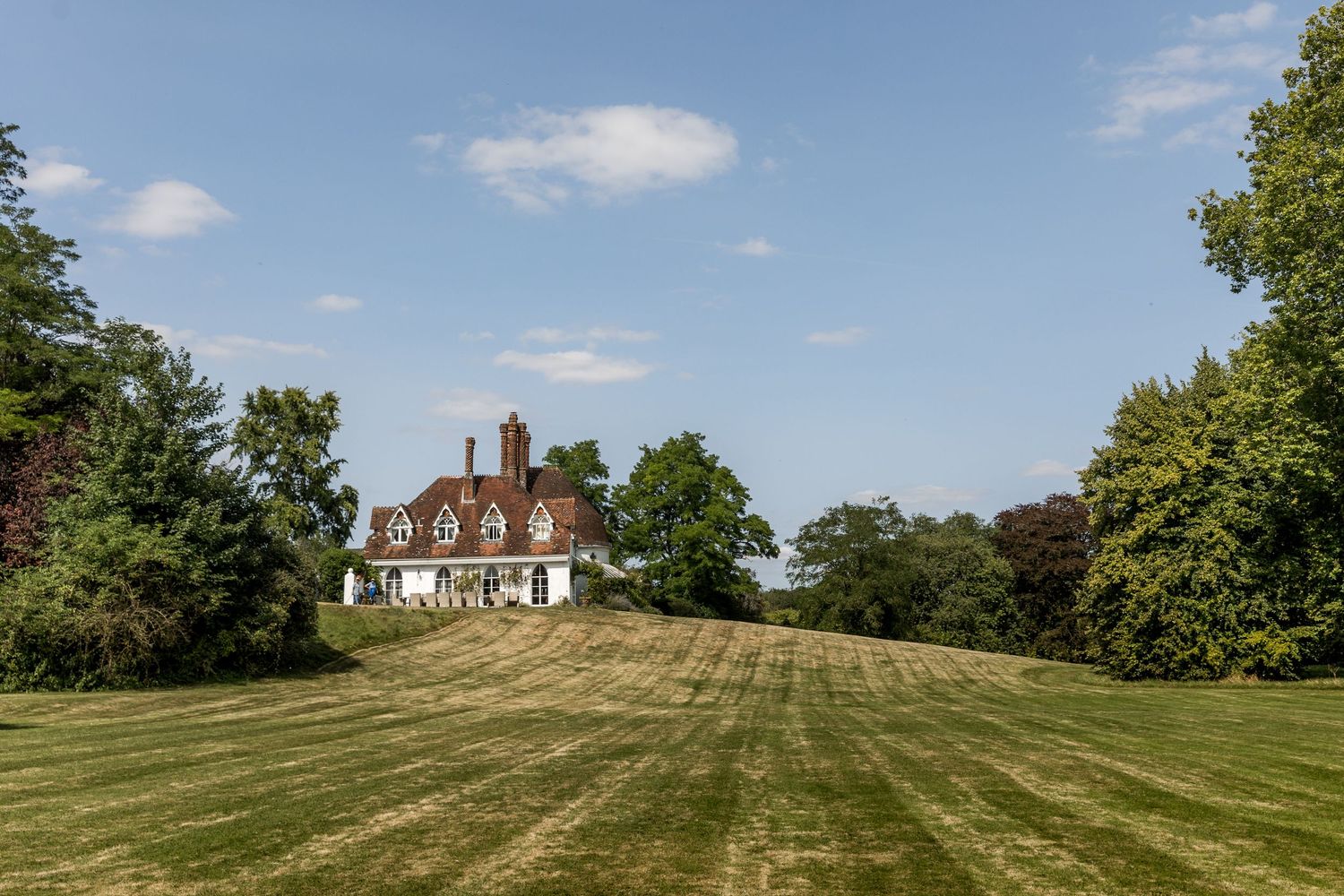 Panoramic view of Houghton Lodge set on rolling green hills under blue sky.