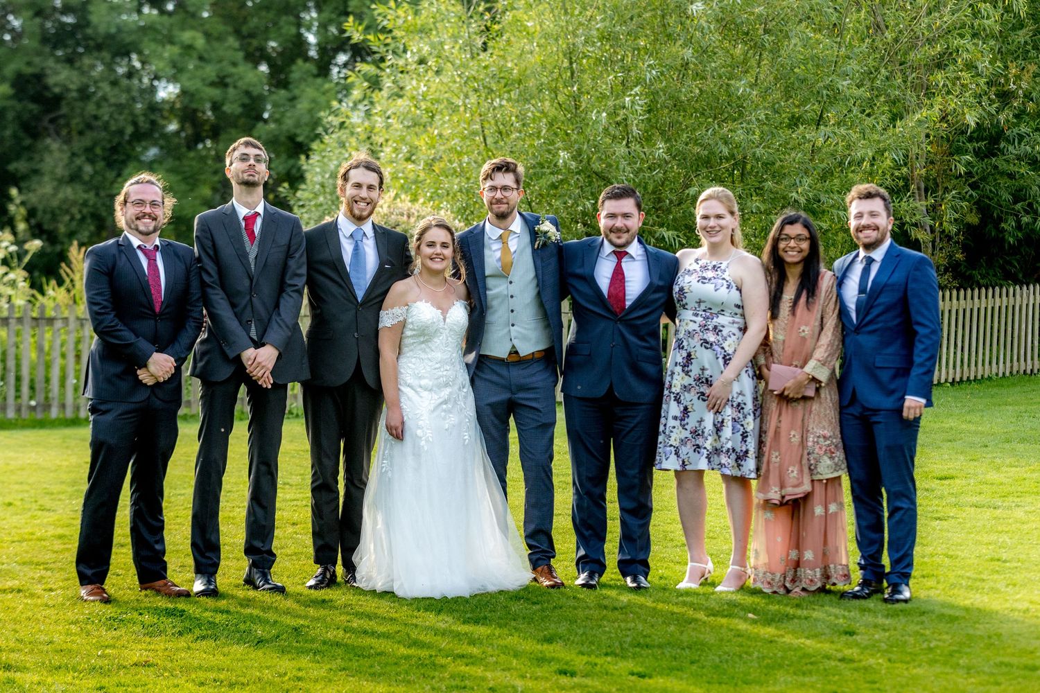 Wedding party poses for formal group photos on a lush green lawn.