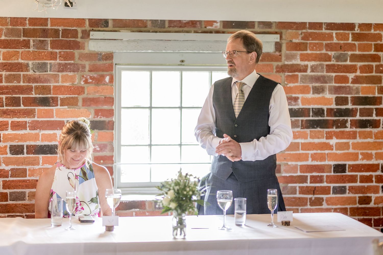 Wedding guests seated at tables in a rustic brick-walled venue during a reception celebration.