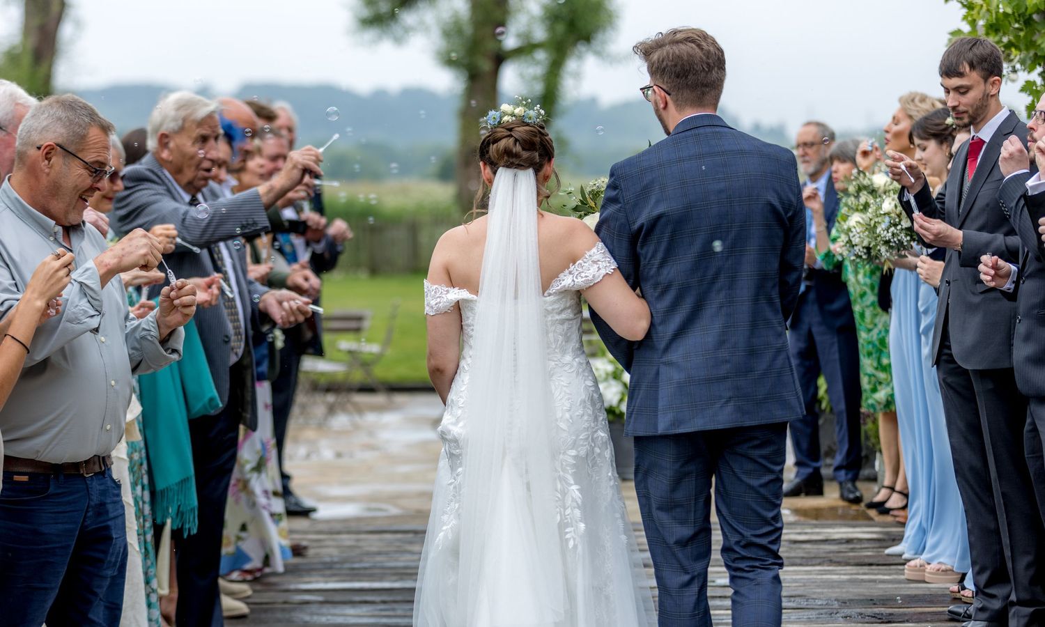 Wedding party and guests mingle during an outdoor reception with lush greenery.