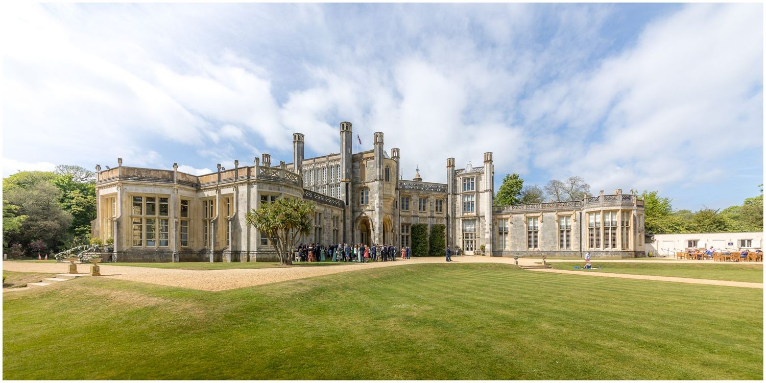 Panoramic view of a grand historic mansion with manicured lawns and gardens on a sunny day.
