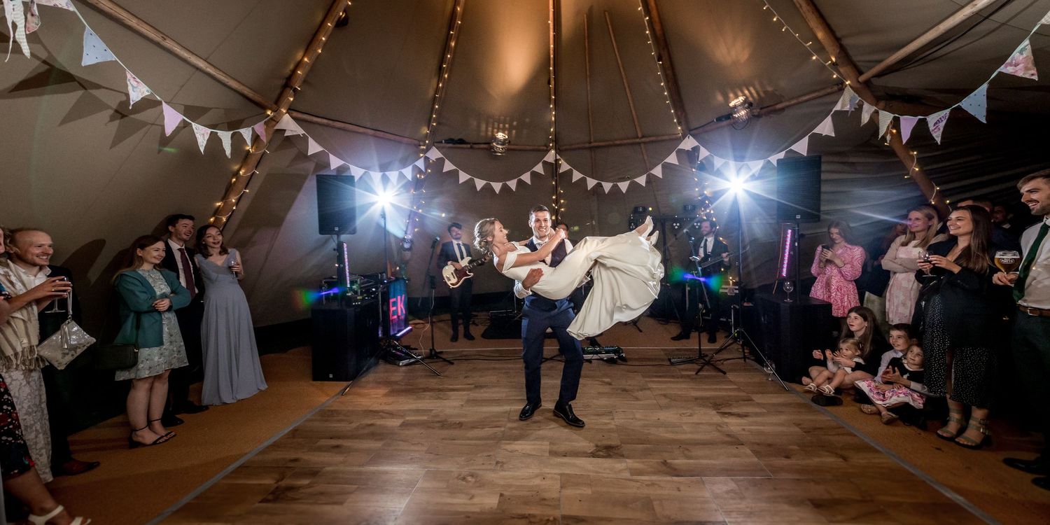 A couple performs a dramatic dance lift in a tent decorated with string lights and bunting.