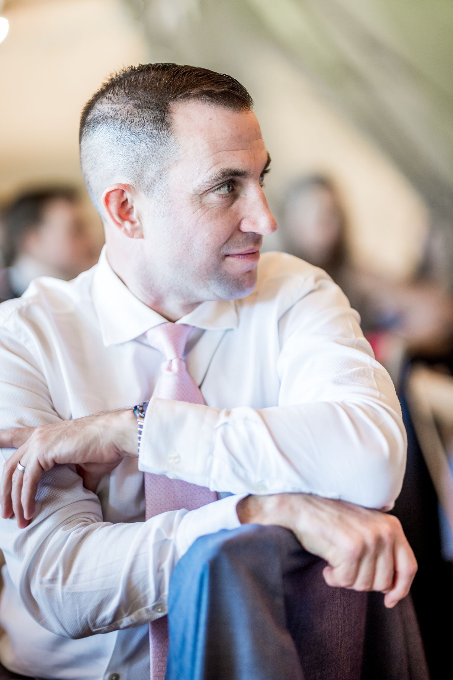 Person in white dress shirt sitting attentively during wedding reception.