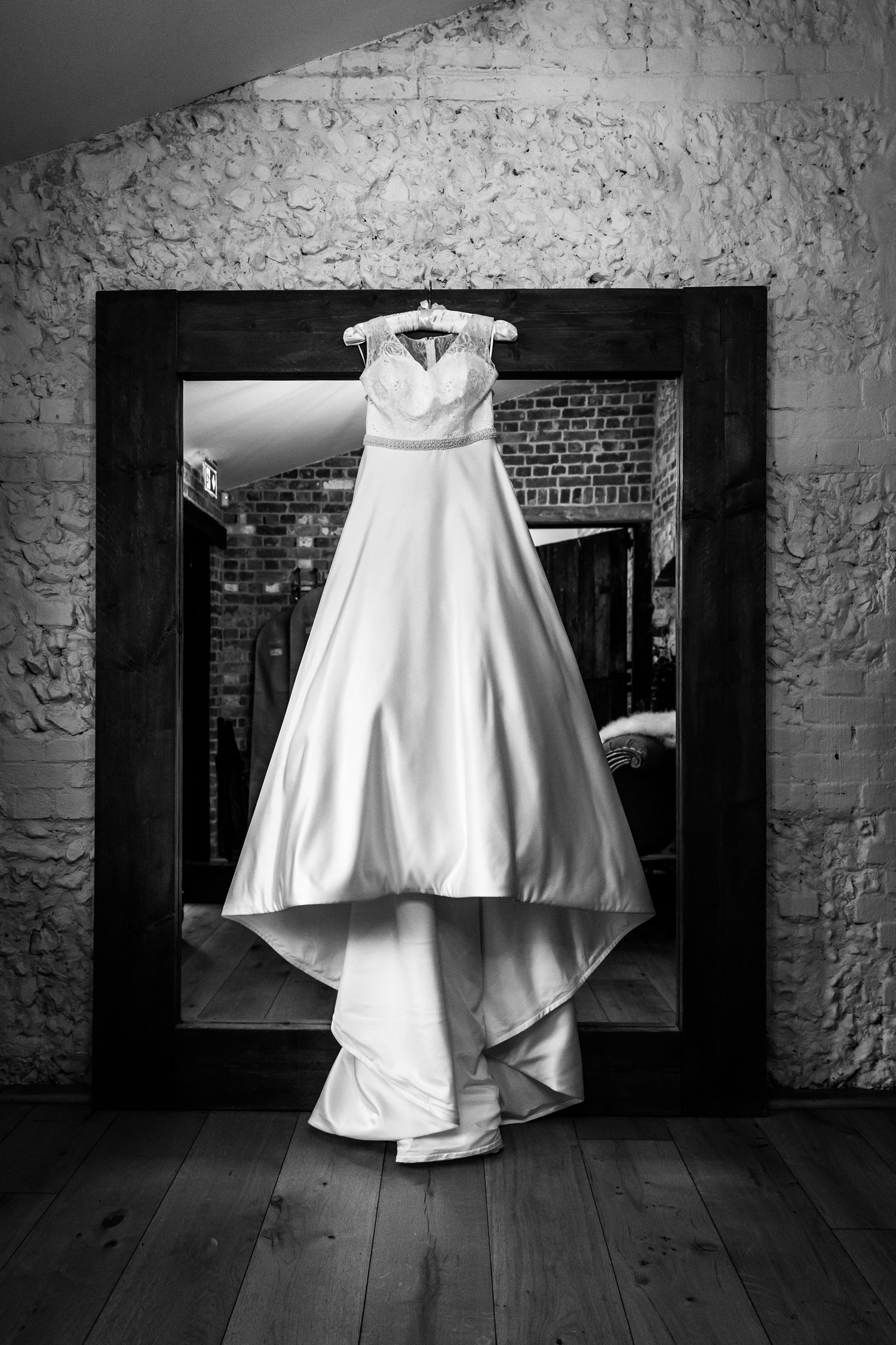 Wedding photography featuring a wedding dress hanging in front of the mirror in the bride's dressing room at Clock Barn, Hampshire