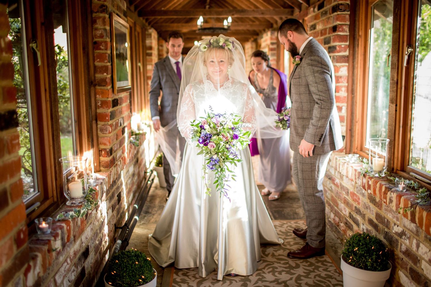 A wedding party poses in a rustic brick-lined walkway decorated with flowers.