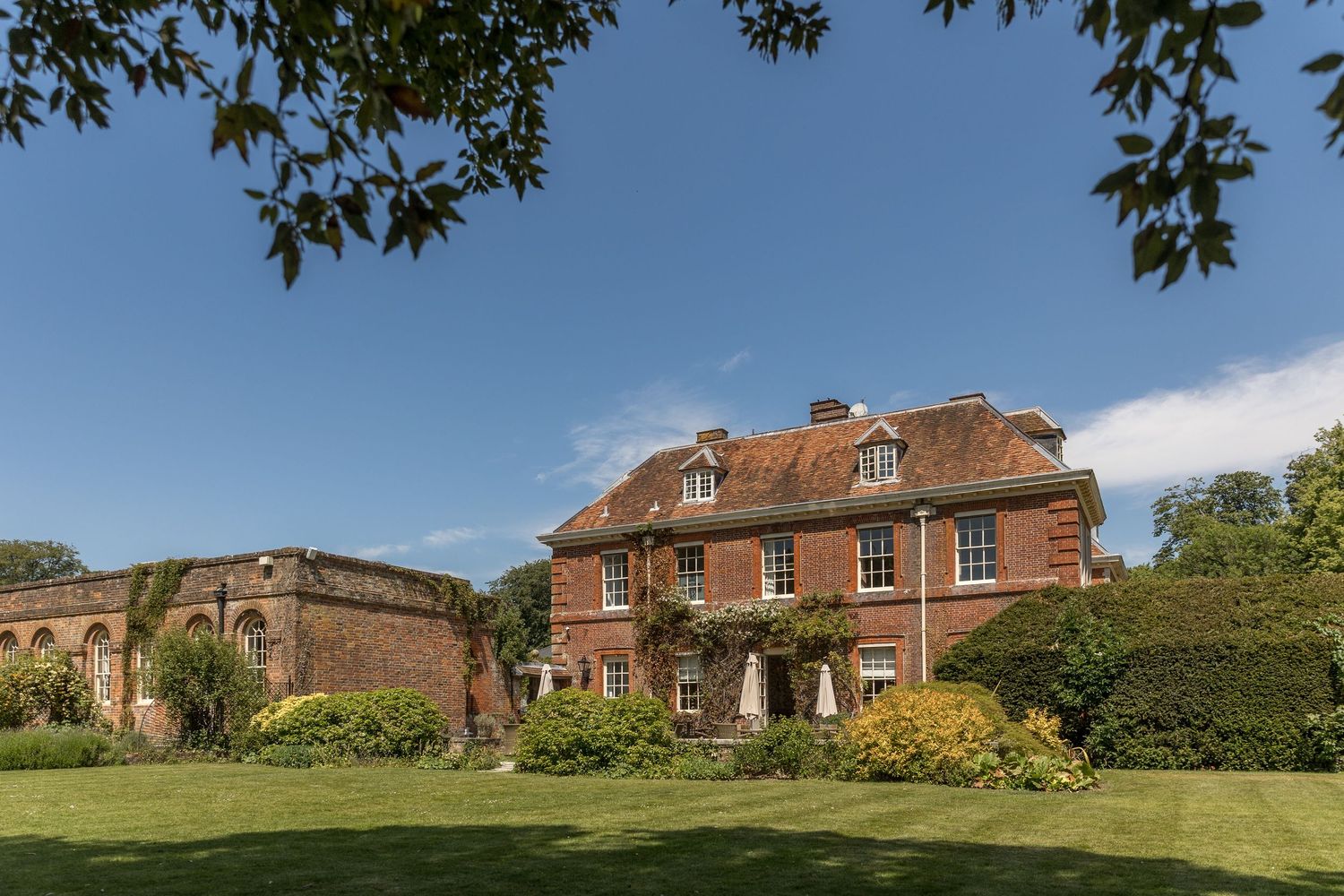 A red brick Georgian country house with dormer windows set in manicured gardens.