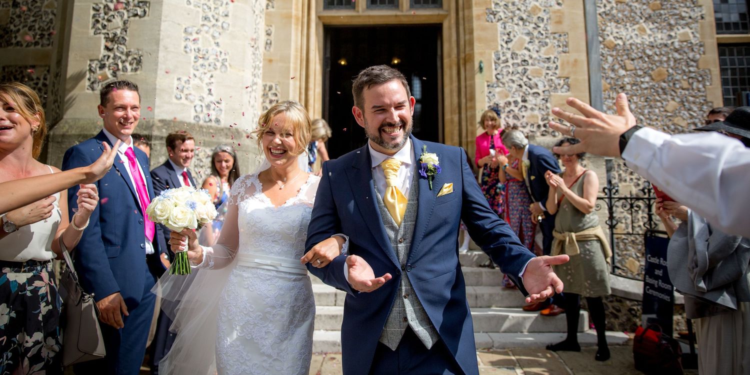 Wedding party celebrates joyfully outside historic stone building during summer ceremony.