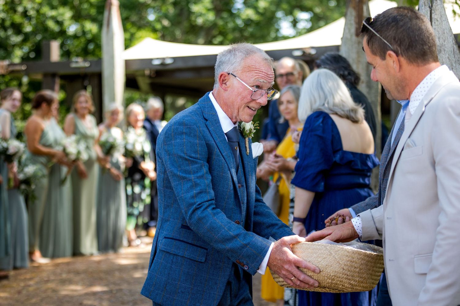 Wedding guests gather outdoors under trees for summer celebration.