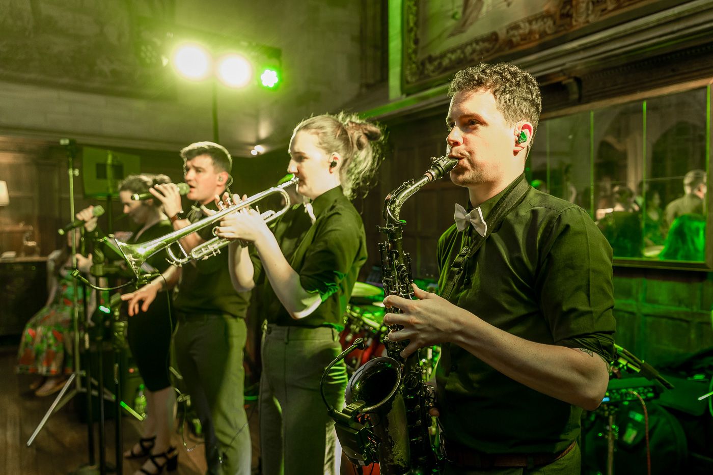 Live band performing on stage with dramatic green lighting and brass instruments.