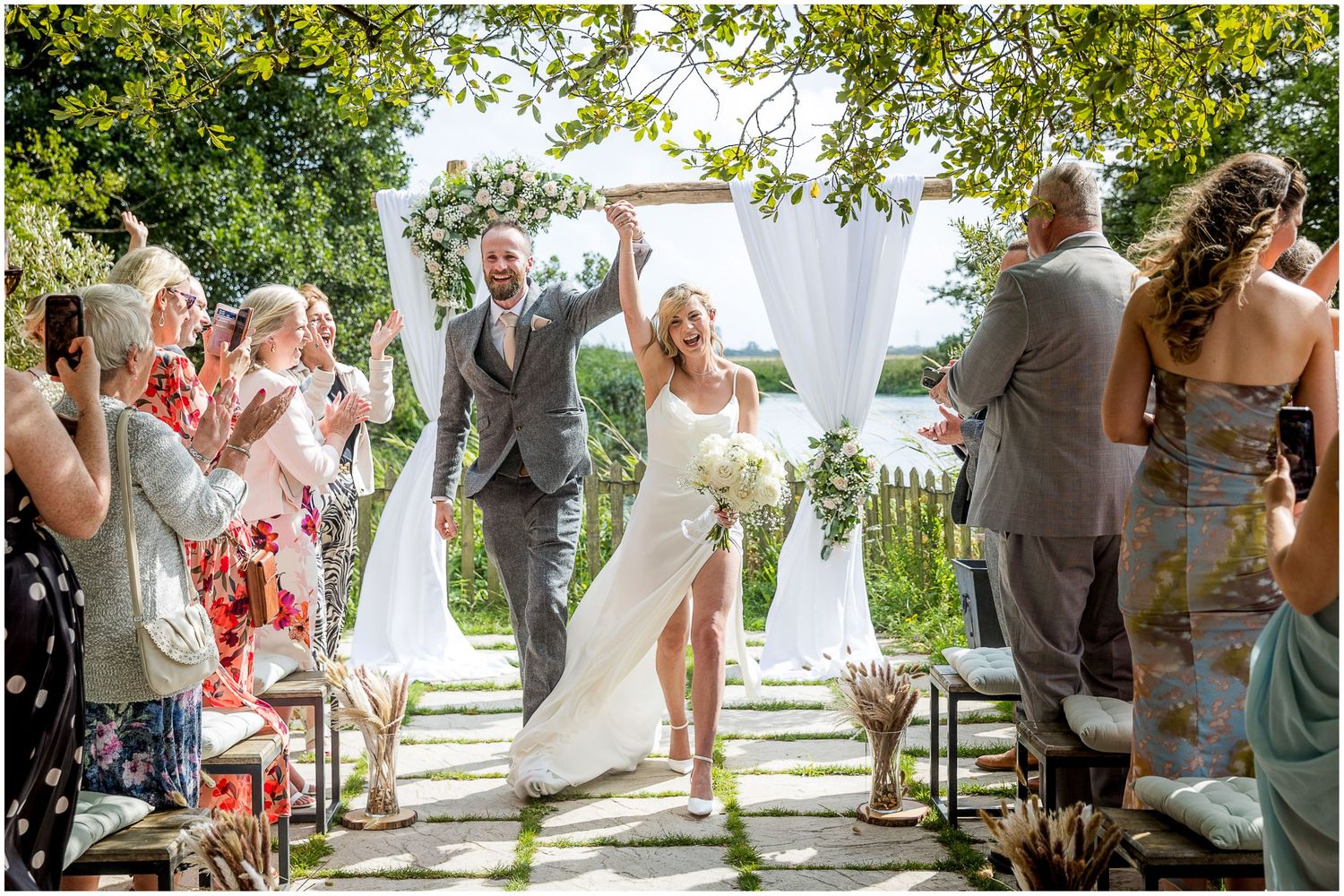 Outdoor wedding ceremony setup with white decor and natural garden backdrop.