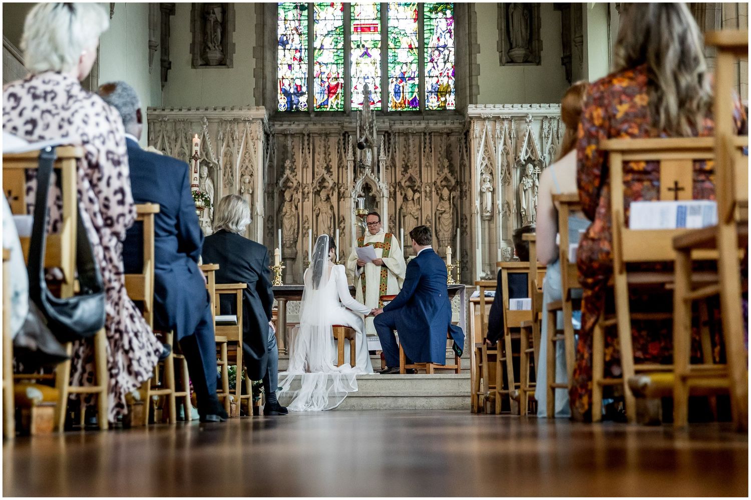 View down the church aisle during a wedding ceremony with guests seated on wooden chairs.