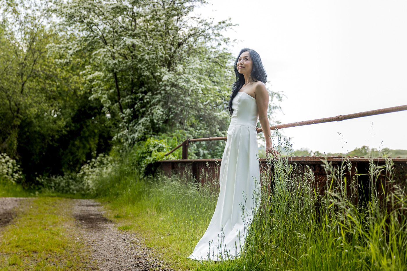 A bride in a flowing white dress poses along a rustic fence surrounded by spring blossoms.