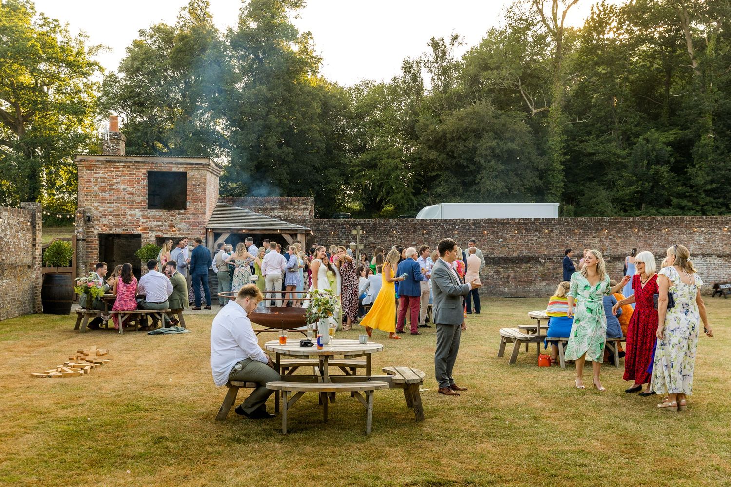 Panoramic view of an outdoor wedding reception with guests gathered around tables at sunset.