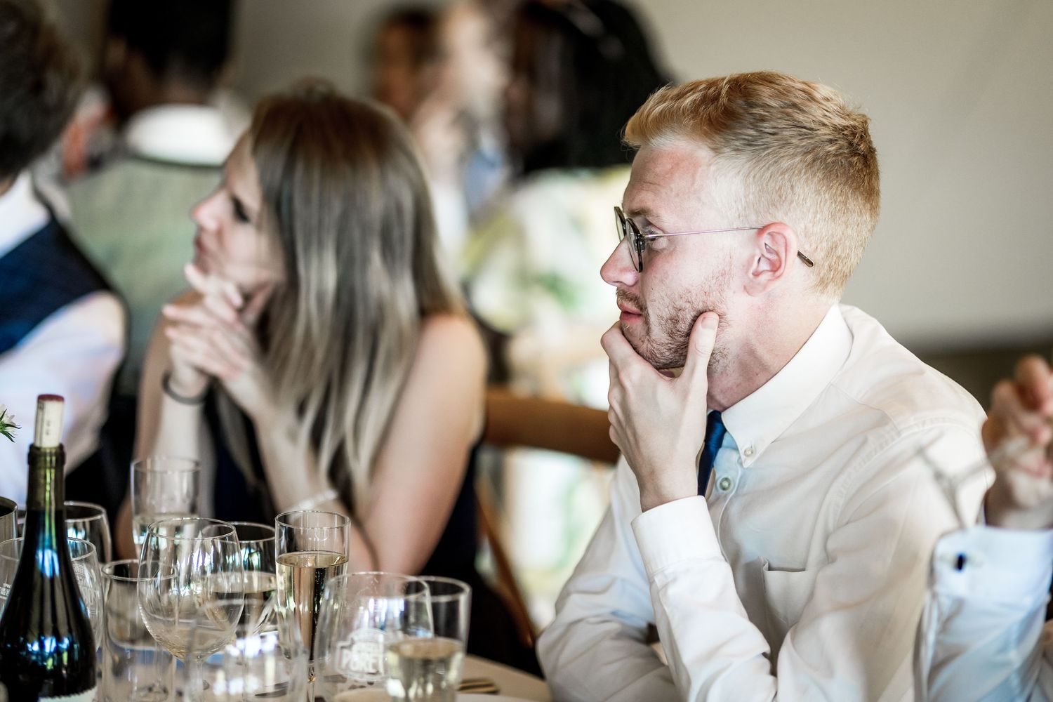 Wedding guests seated at long tables during reception speeches.