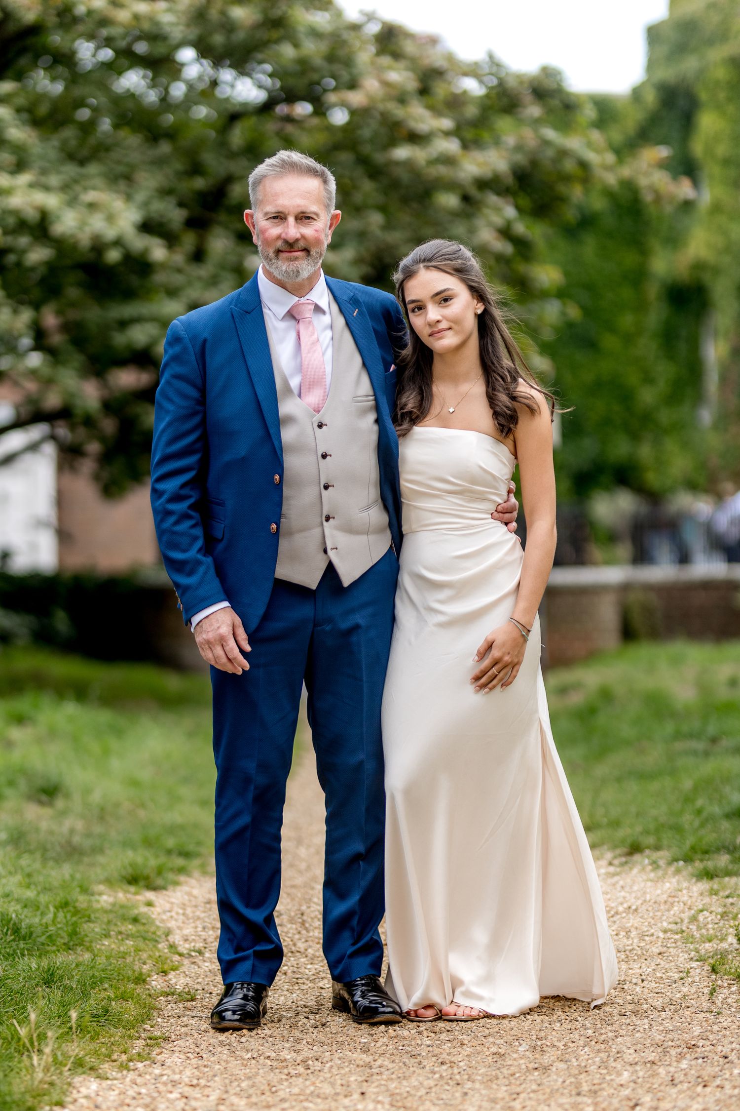 Wedding couple walks hand in hand along gravel path surrounded by lush greenery.