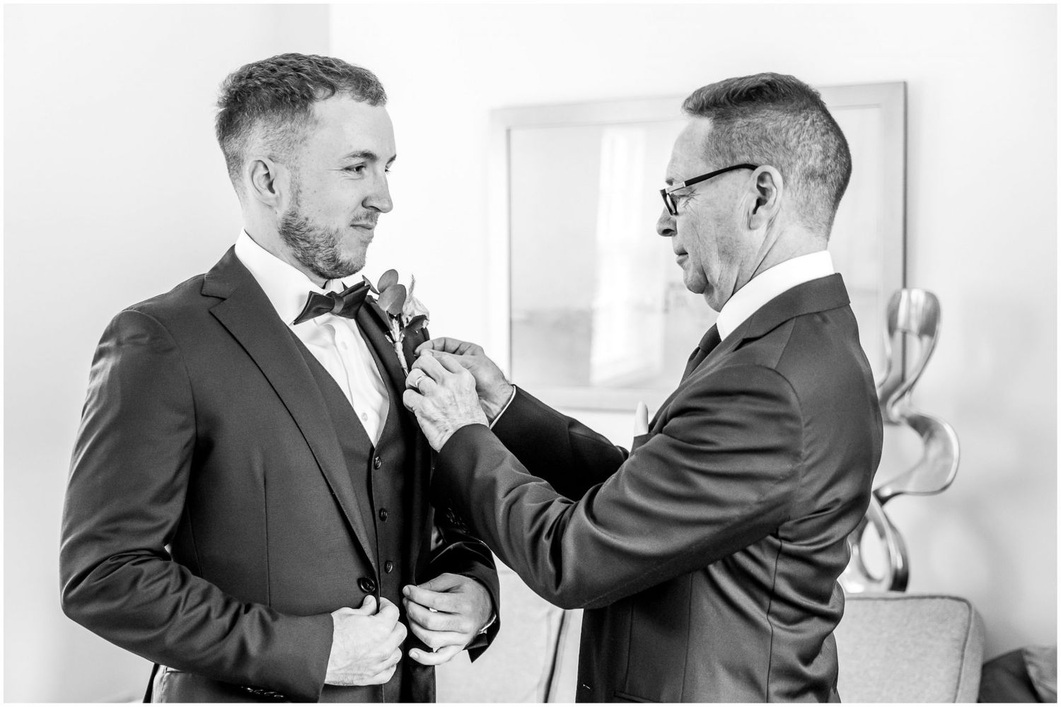 Black and white photo of two people in suits adjusting their formal attire.