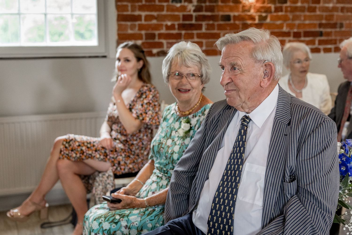 Wedding guests seated in rows at a venue with exposed brick walls and natural lighting.
