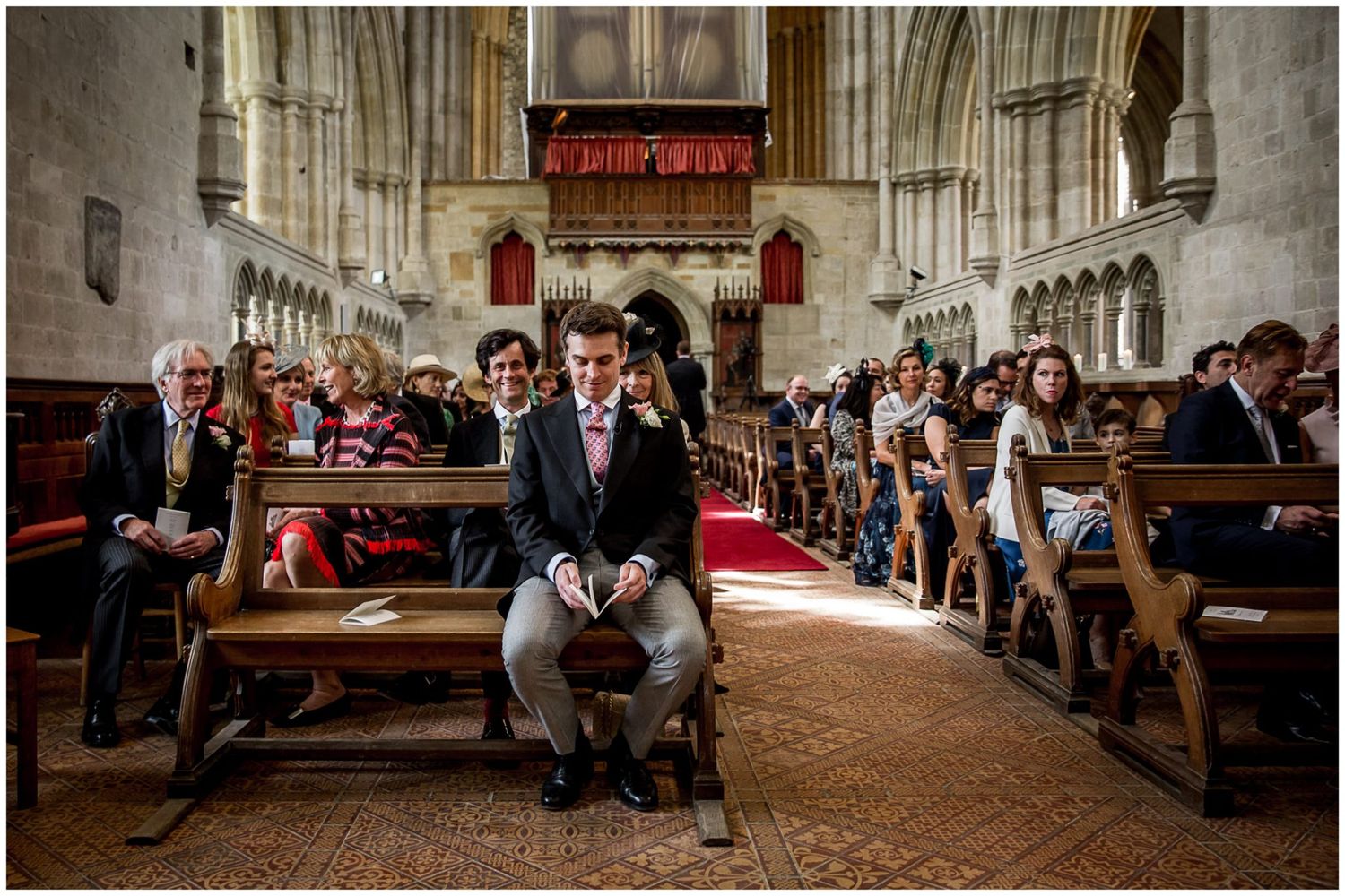 People sit in wooden church pews during a traditional wedding ceremony in a historic stone chapel interior.