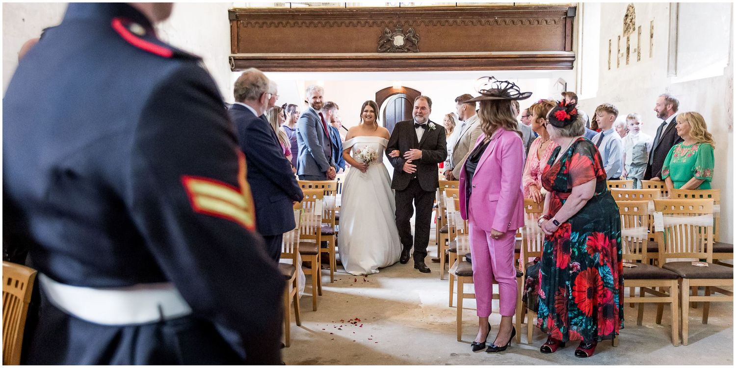A wedding ceremony in progress inside a bright white room with guests seated in wooden chairs.