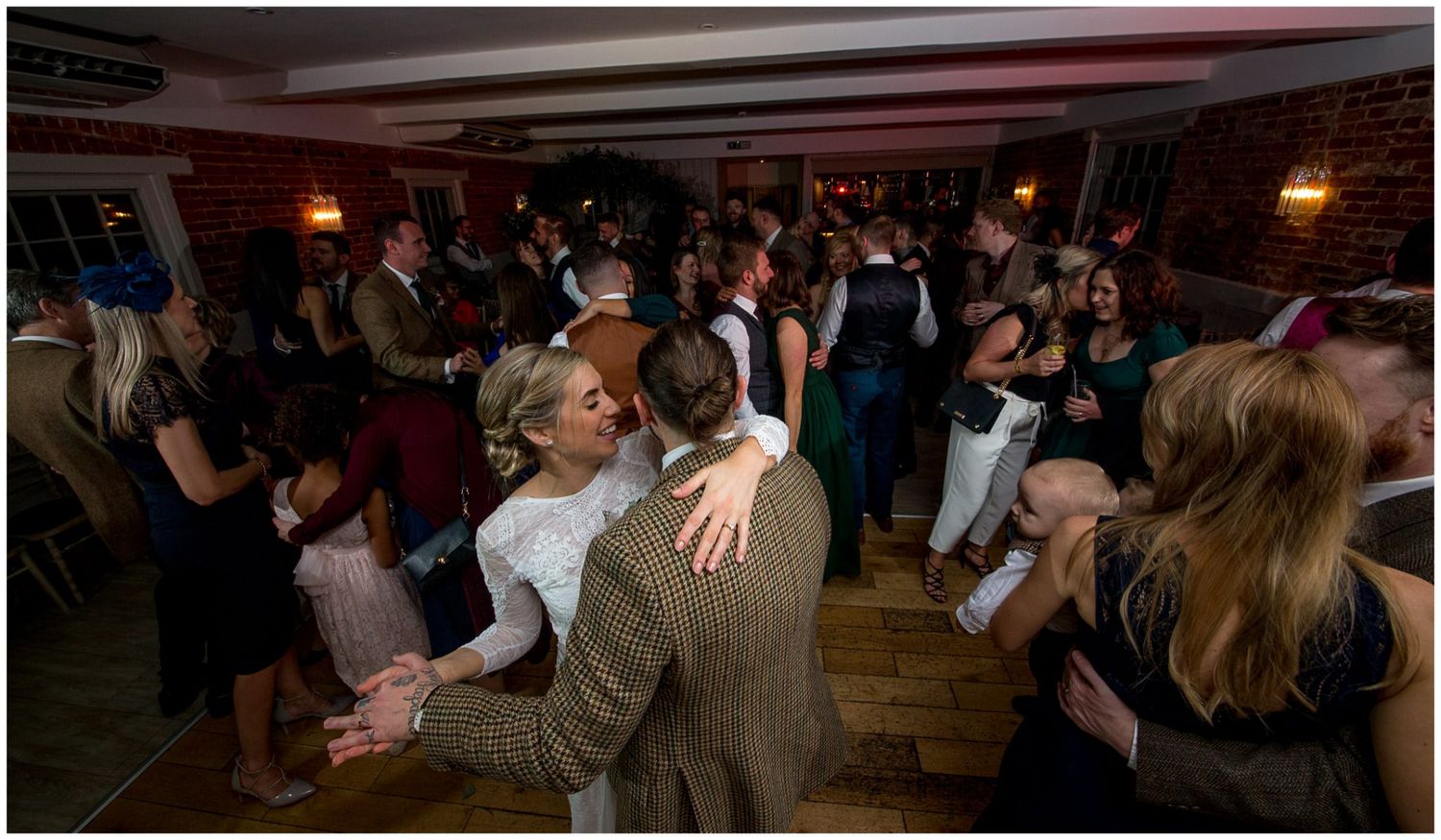 Wedding guests dancing and celebrating on a dimly lit dance floor with warm lighting.