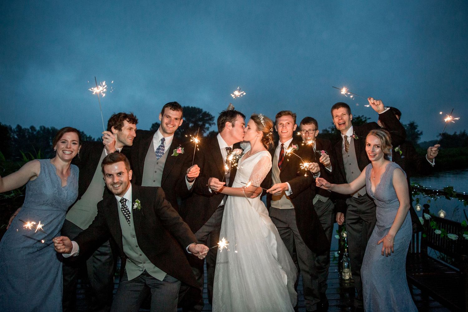 Wedding party celebrates with sparklers at dusk during outdoor reception celebration.