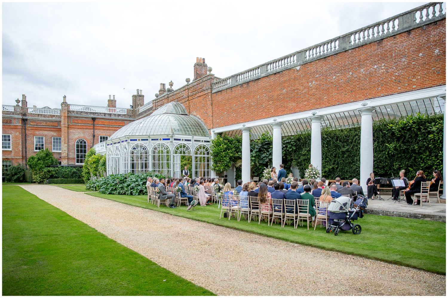 Panoramic view of wedding guests seated for outdoor ceremony at historic brick venue.