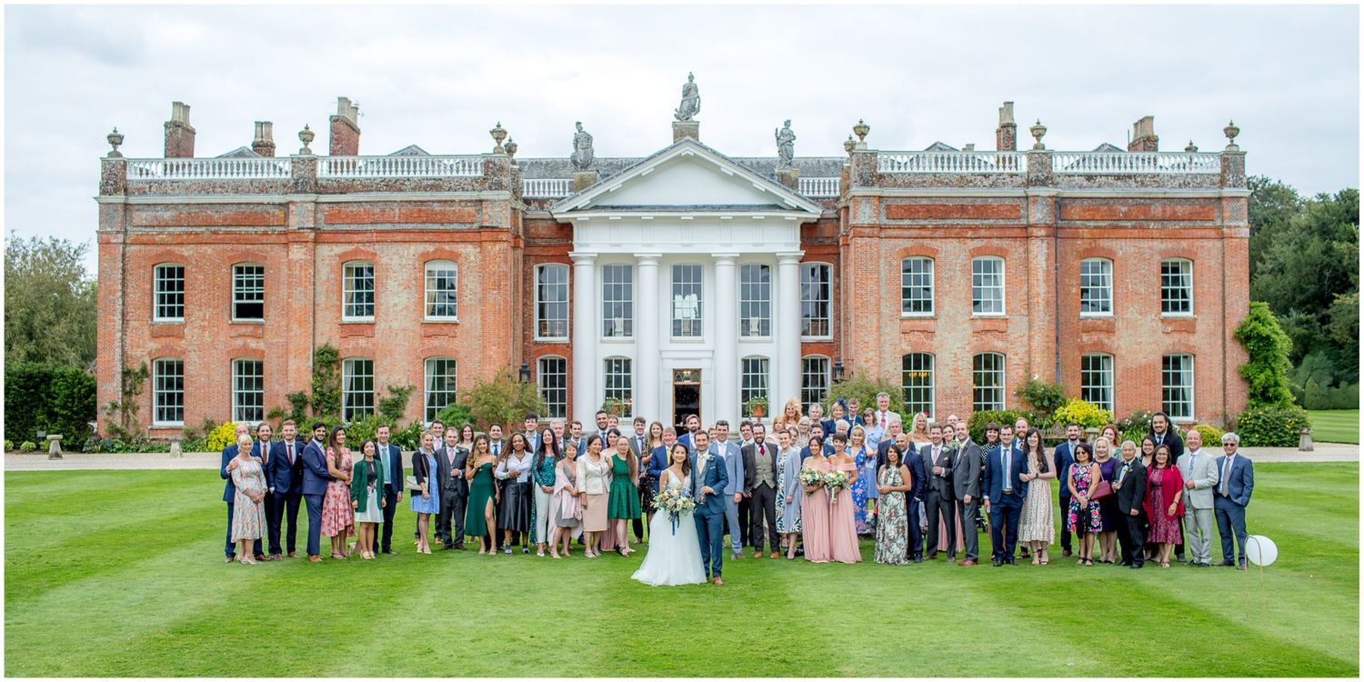 Large group photo of wedding guests in front of grand historic mansion with white columns.
