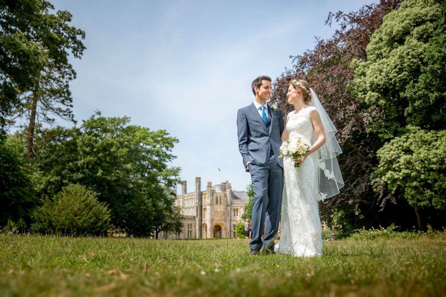 Bride and groom stood in the grounds of Highcliffe Castle in the sunshine, with the New Forest wedding venue in the background