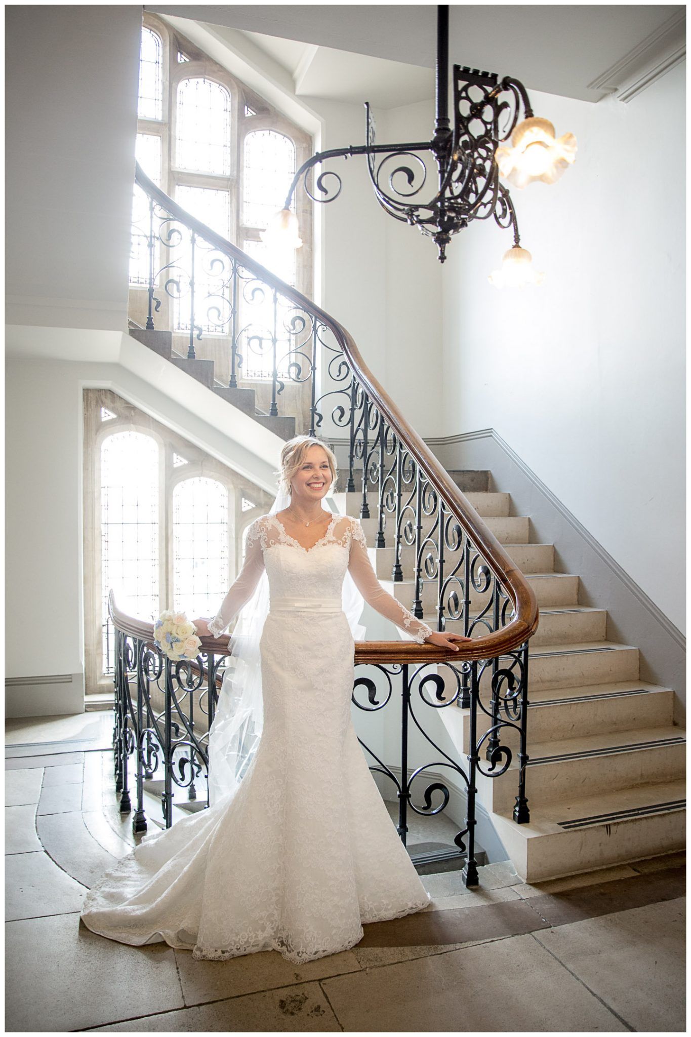 A wedding dress flows elegantly across a grand staircase with ornate black wrought iron railings in a bright white interior.