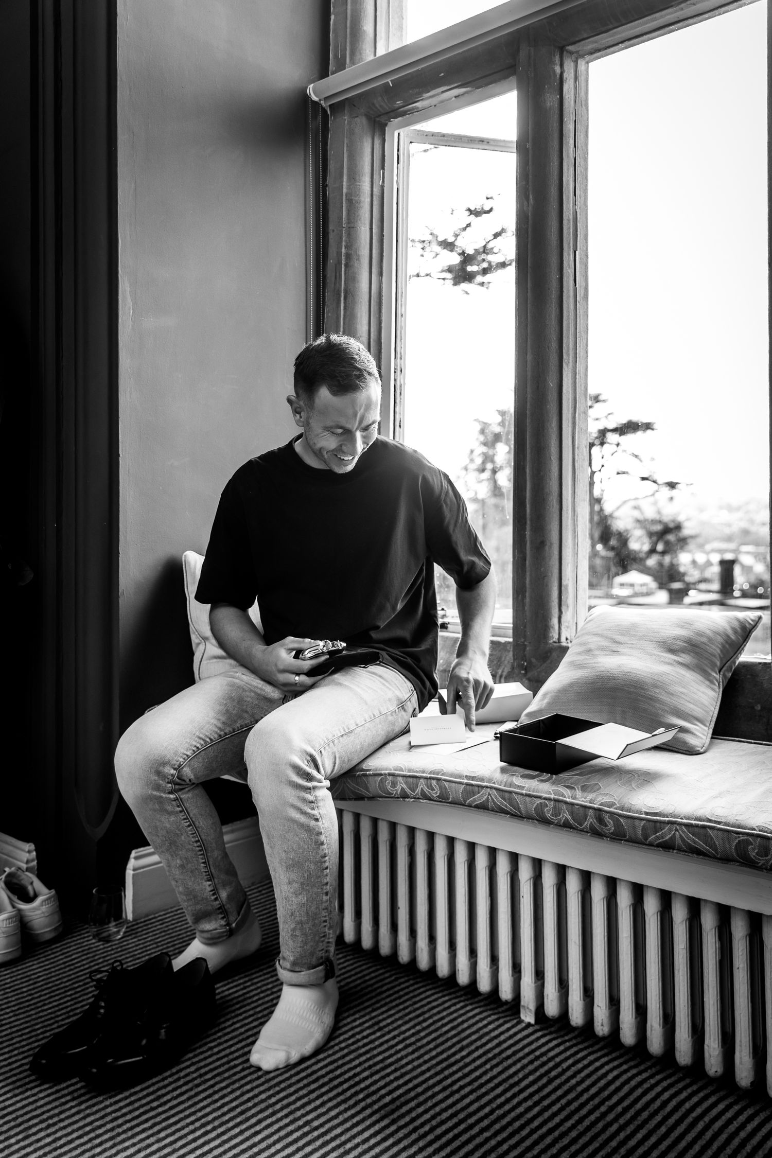 Black and white photo of person sitting on window seat looking at device.
