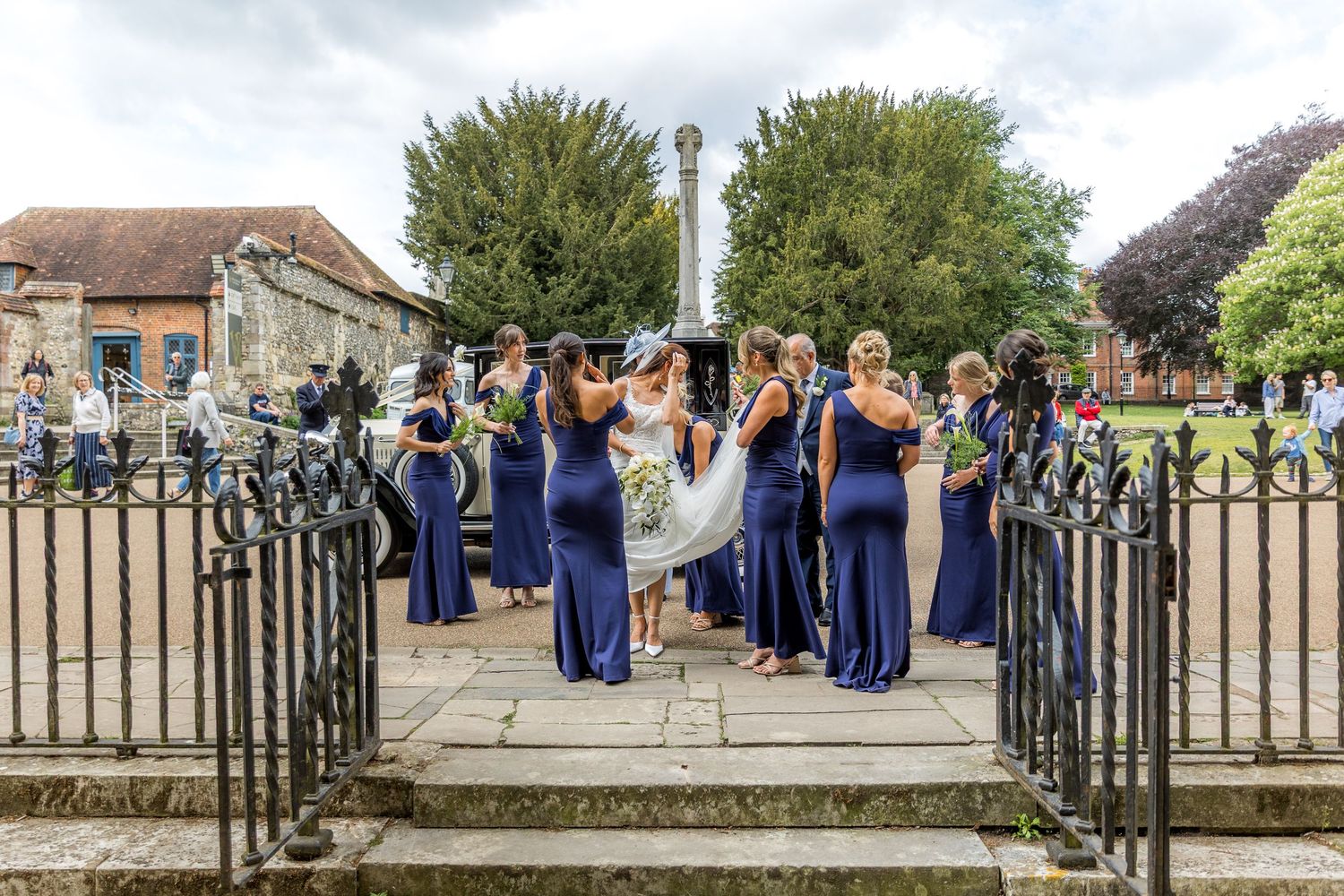 Wedding party in navy blue poses along an ornate iron fence outdoors.