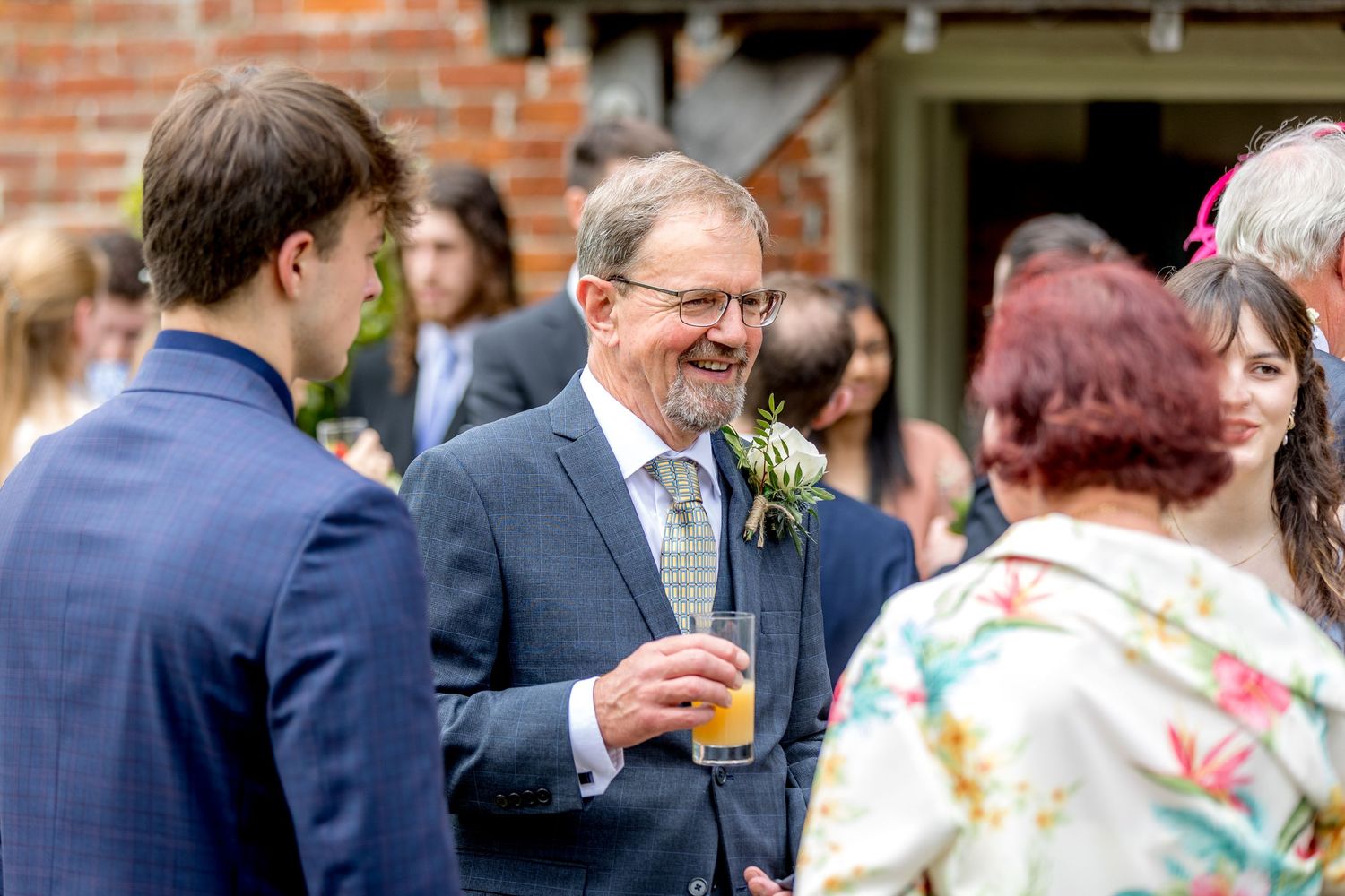 Wedding guests mingling at an outdoor reception near a brick building.
