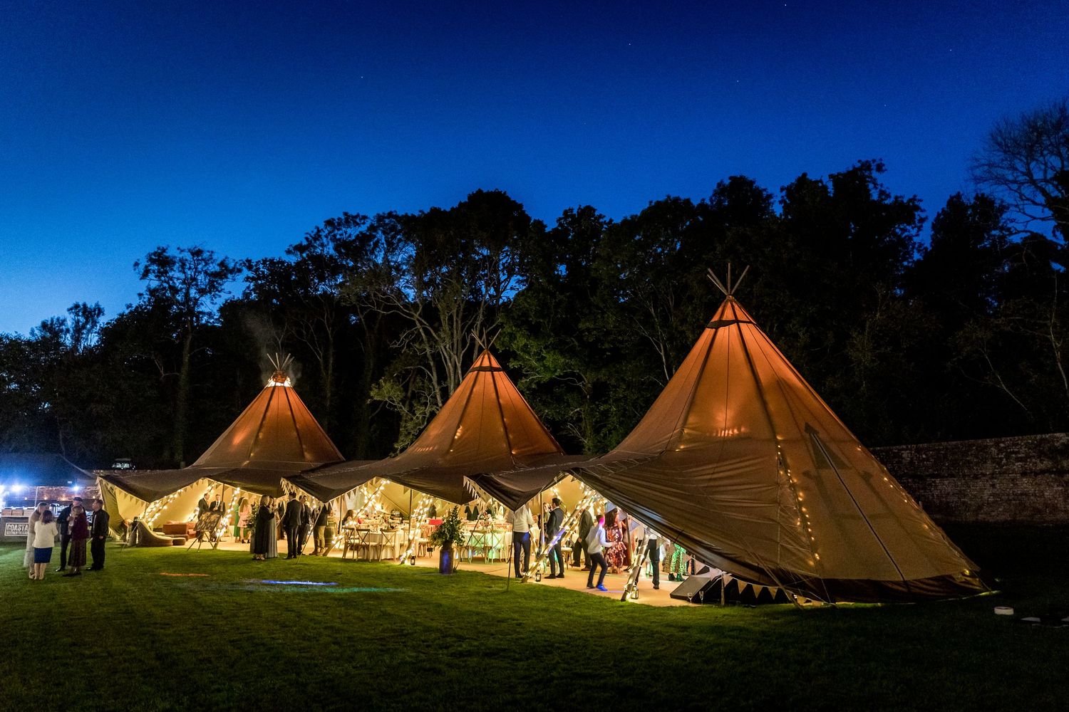 Illuminated tipi-style tents glowing at dusk during an outdoor event.