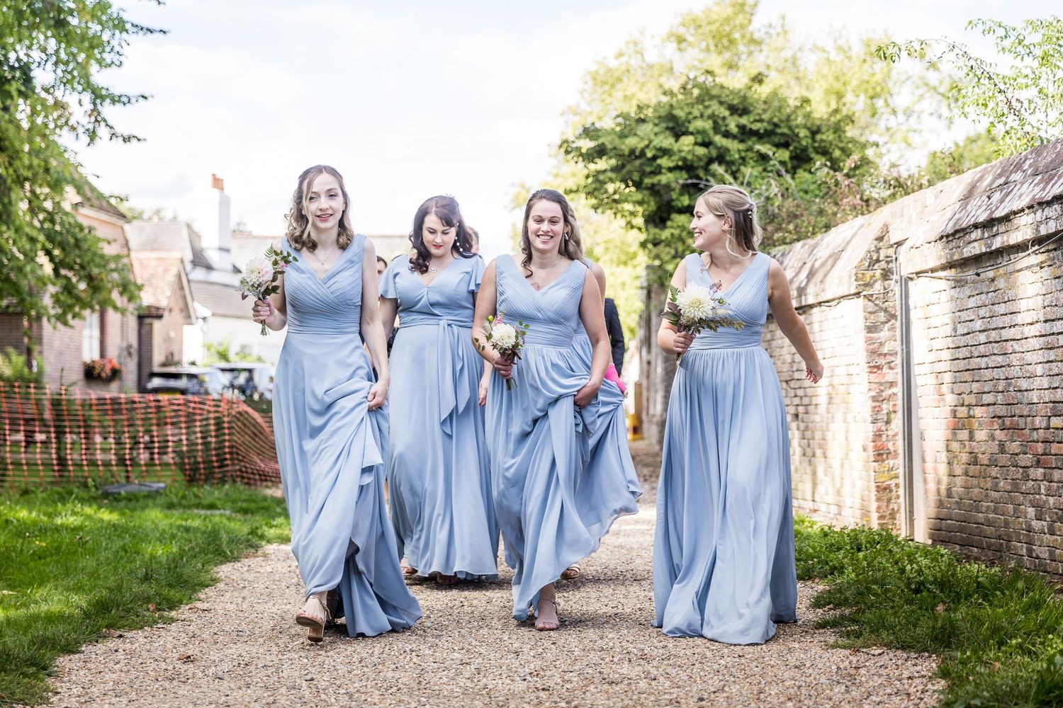 Bridesmaids in light blue dresses walking together through garden pathway.