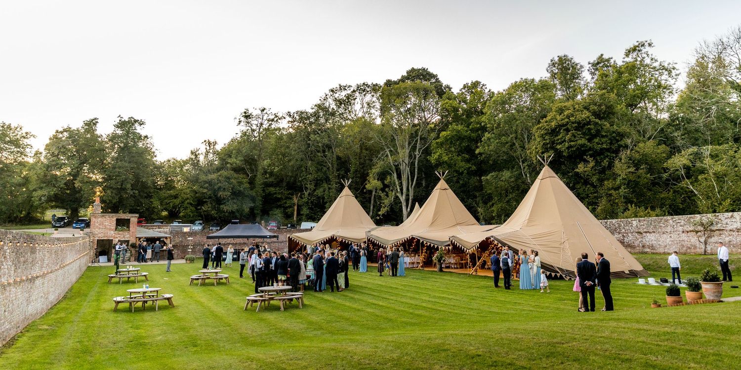 Panoramic view of a wedding venue with tipi tents set up on a sprawling green lawn.